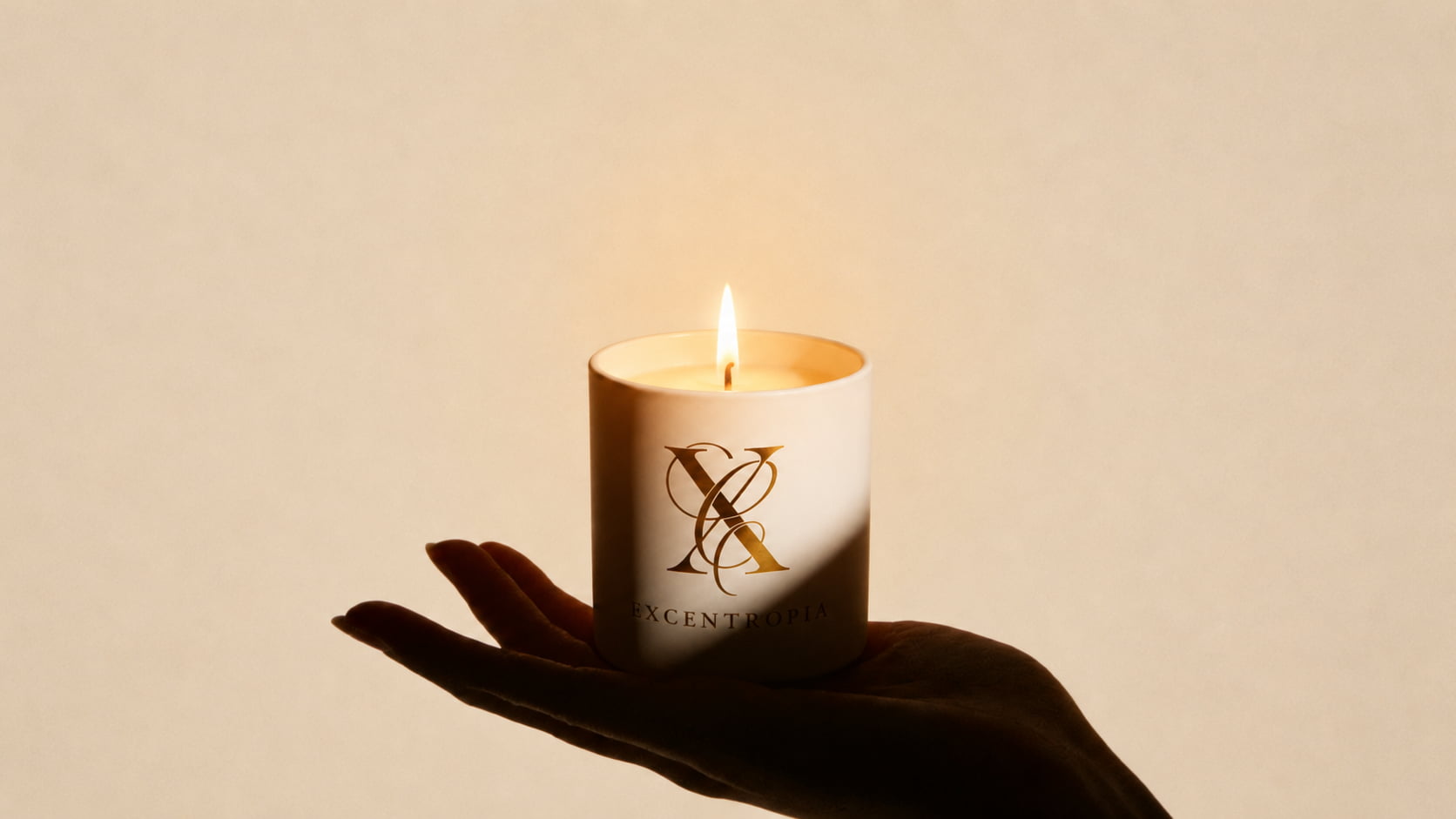 Vela aromática artesanal Excentropía encendida sobre una mano con iluminación cálida.